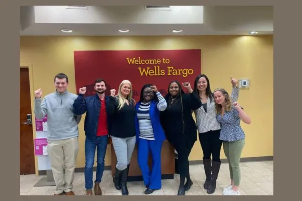 7 Wells Fargo employees in stand in front of sign with fists raised